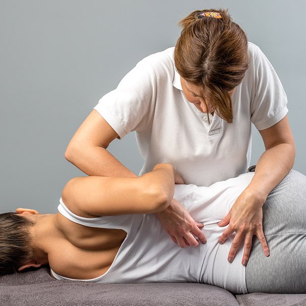 Female physiotherapist doing manipulative spine treatment on young patient.